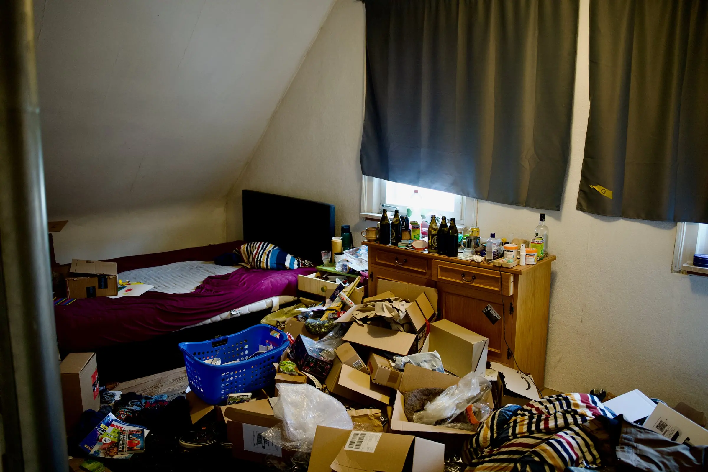 Messie-Haushalt vor der Räumung – Schlafzimmer unter der Dachschräge, der Boden voller Kartons, Flaschen und Hausrat